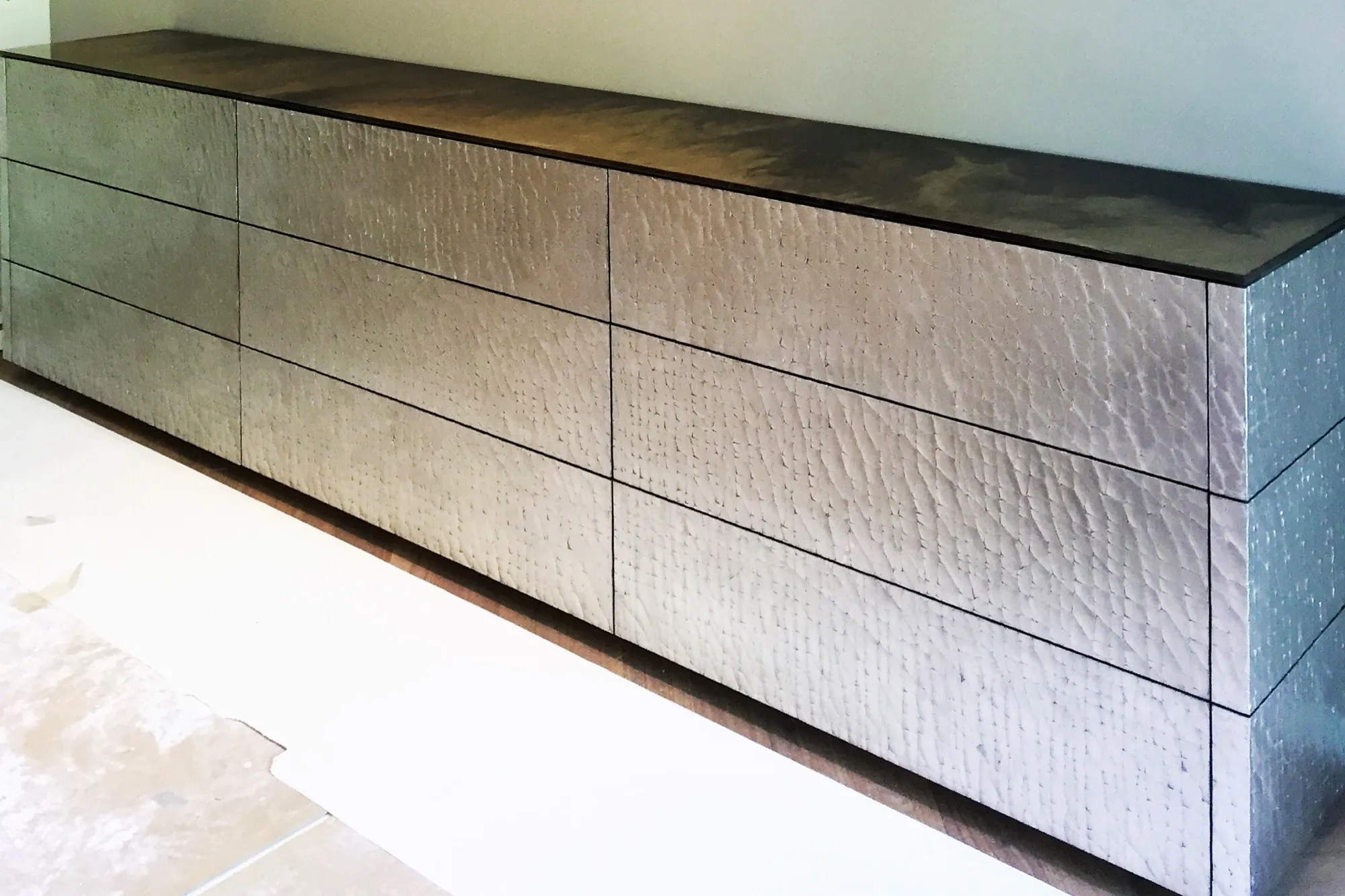 Sideboard mit silbrig schimmernder, fein strukturierter Furnier-Oberfläche an der Wand