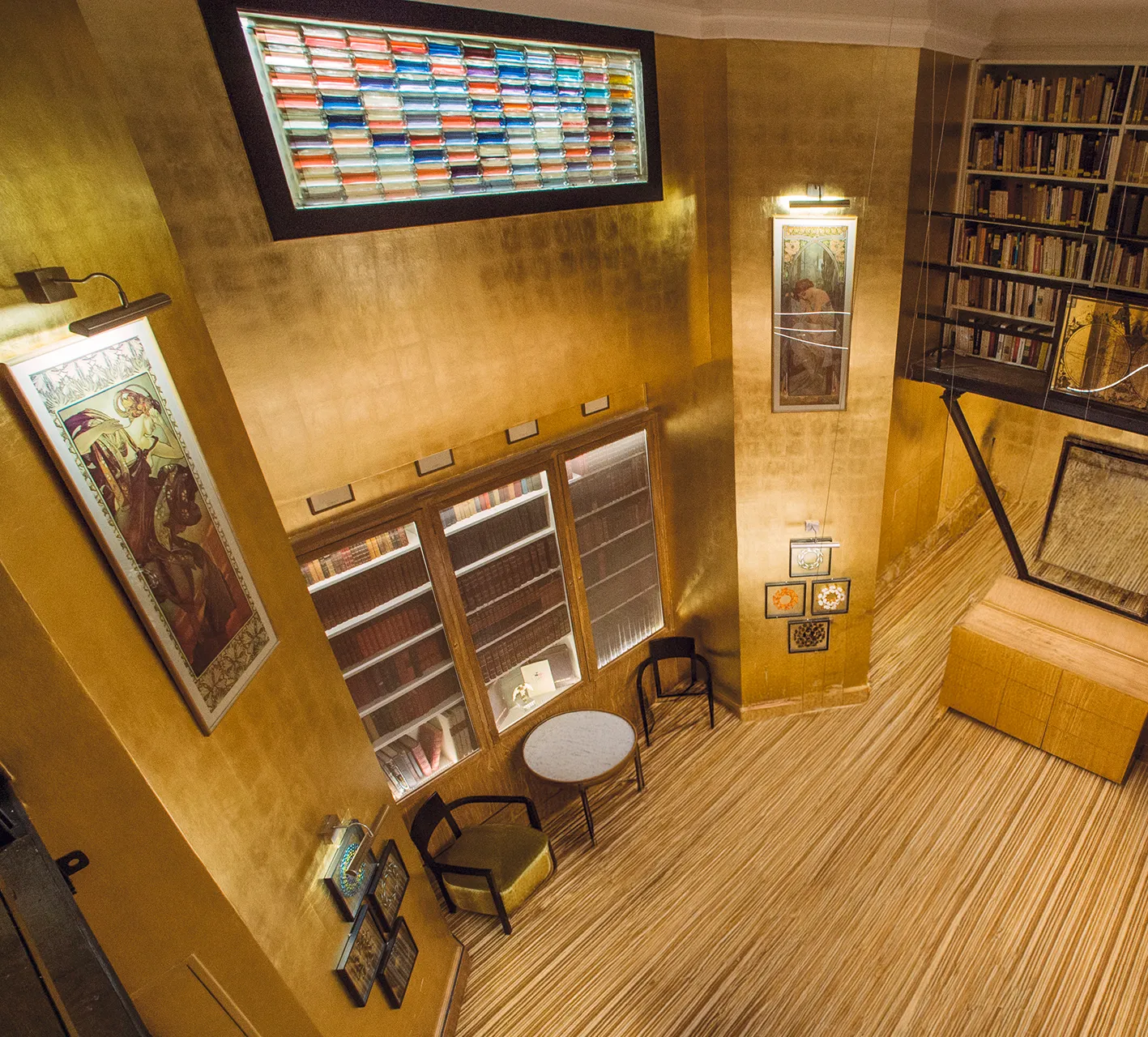 Zweigeschossiger Hotelbibliotheksraum mit gold-metallischen Wänden, Bücherregalen und farbigem Buntglas-Lichtband