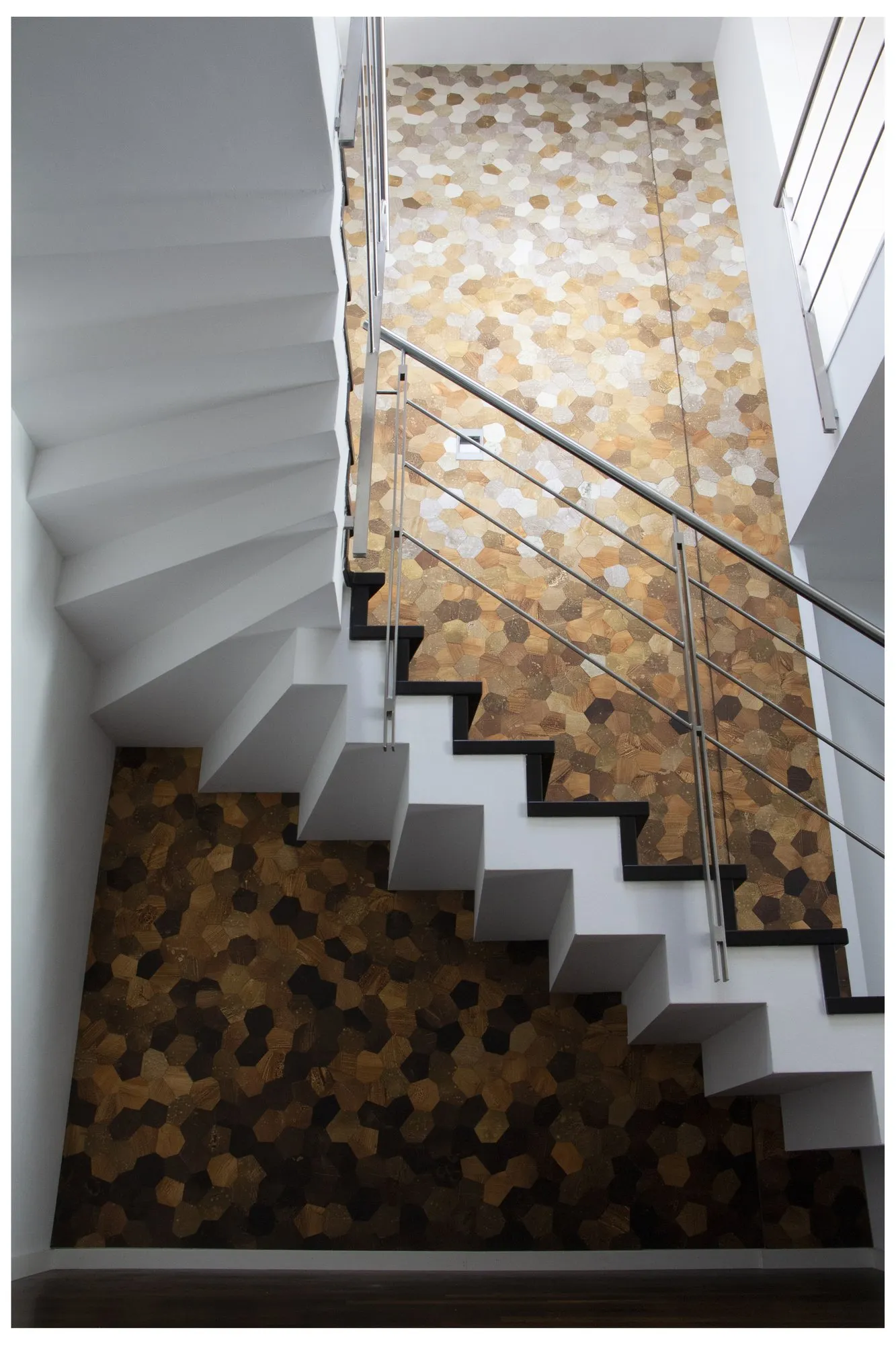 Treppenhaus mit zwei Wandflächen aus Hexagon-Mosaik, oben in Goldtönen, unten in dunkler Bronze