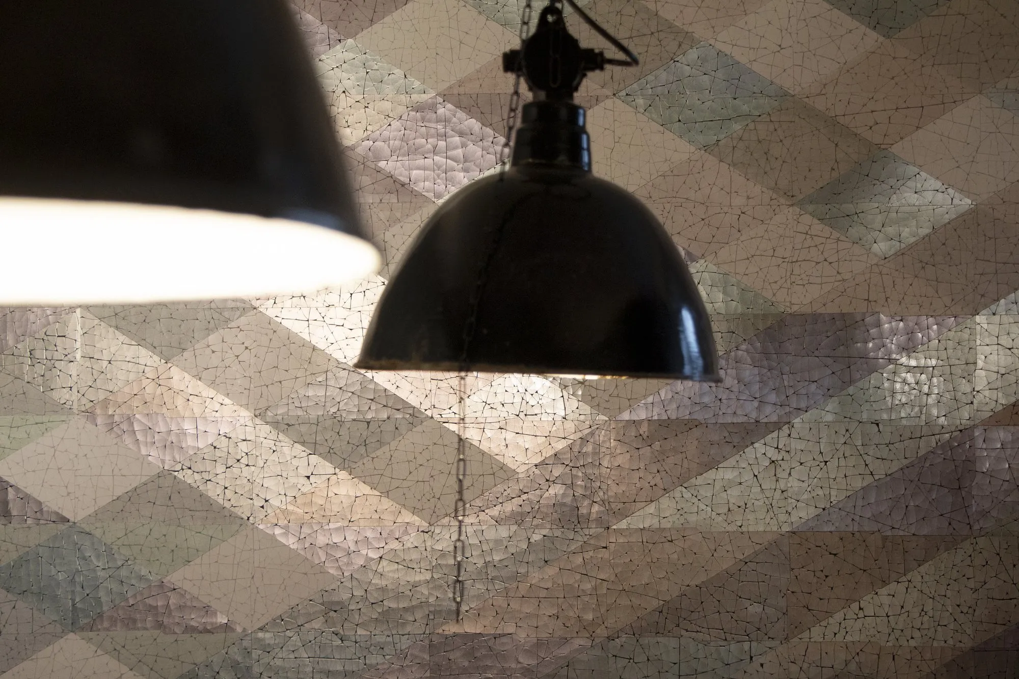 Wandbild aus großformatigen Krakelee-Dreiecken in zartem Beige- und Greigeton mit dunkler Industrieleuchte