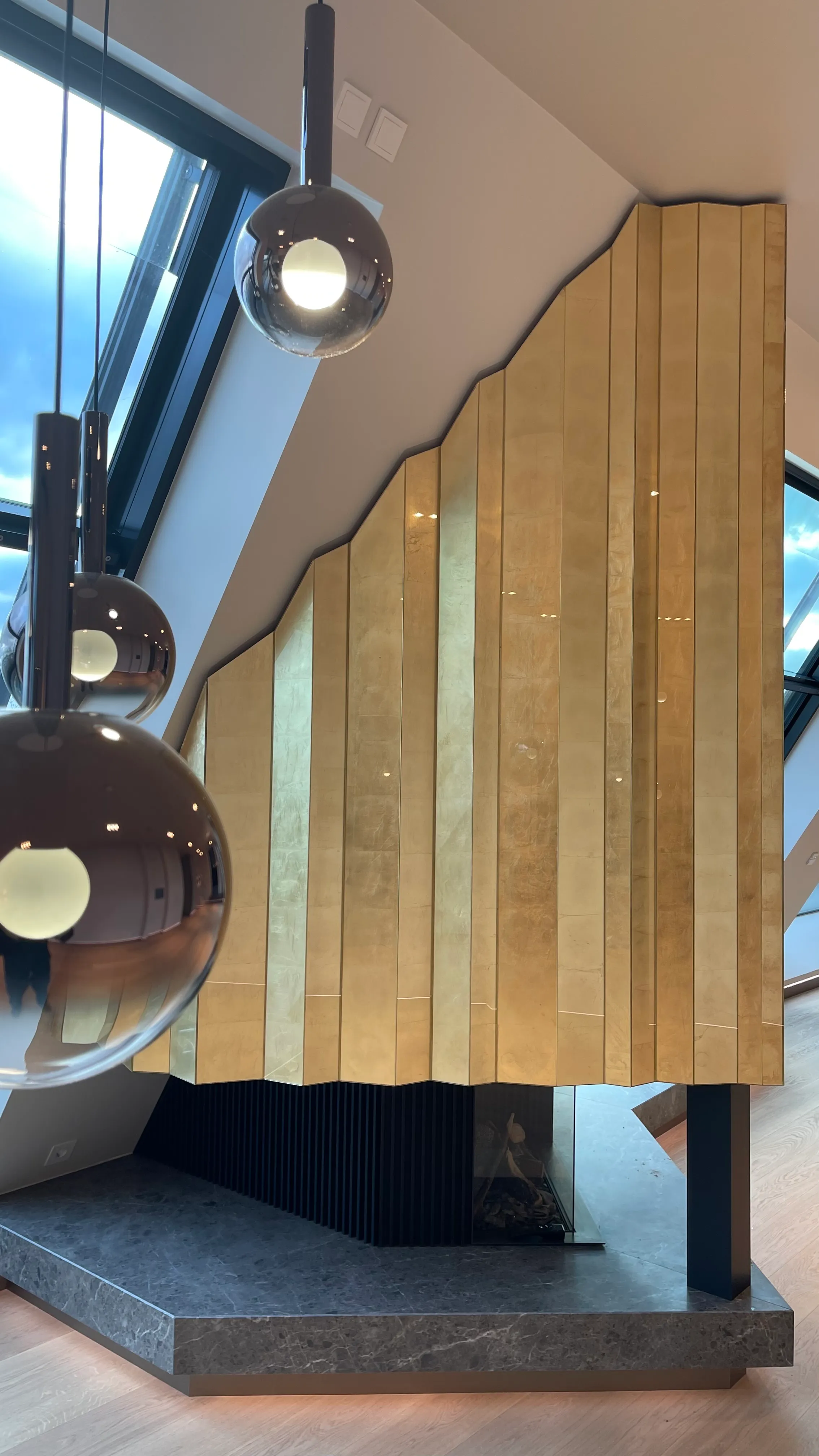 Vertikal gegliederte Kaminwand aus handappliziertem Blattgold